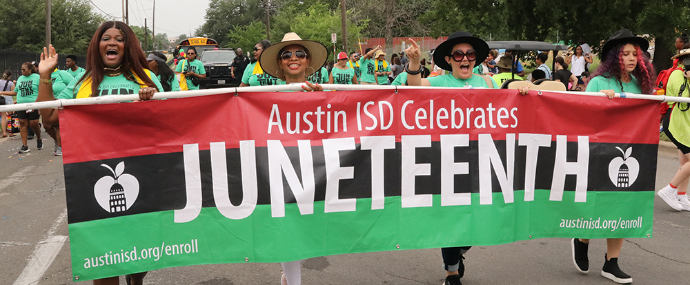 Community marching in the parade on the street holding a Juneteenth banner. Yelling in celebration.