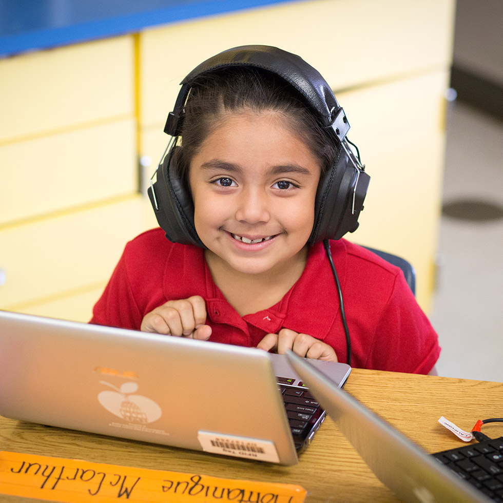 student smiling with headphones on and sitting at a laptop computer